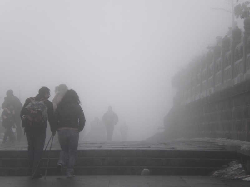 Several people are visible walking on wide stone steps shrouded in thick fog, with a railing visible on the right.