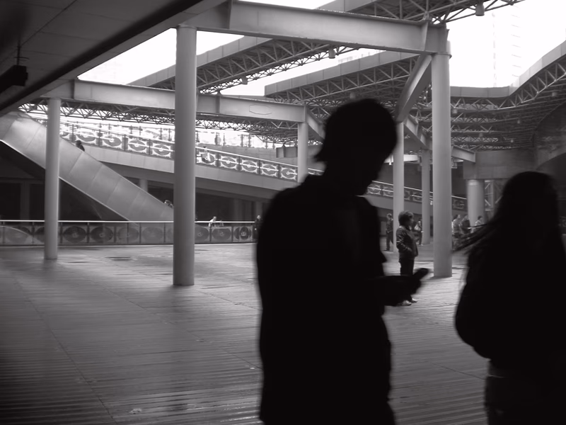 A black-and-white photograph of a modern building with people walking in the shadows.