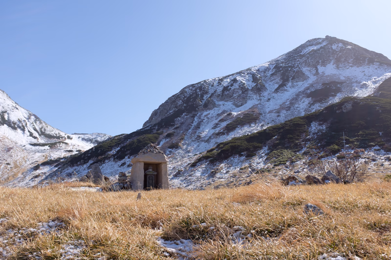 A small hut stands in a snowy, mountainous landscape.