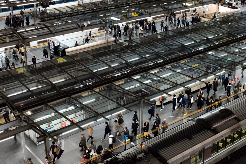 A high-angle view of a busy, multi-level train station platform with many people moving around the covered area.