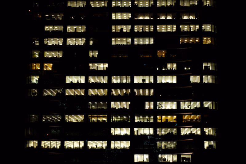 A photo of an office building at night with many windows showing light inside.