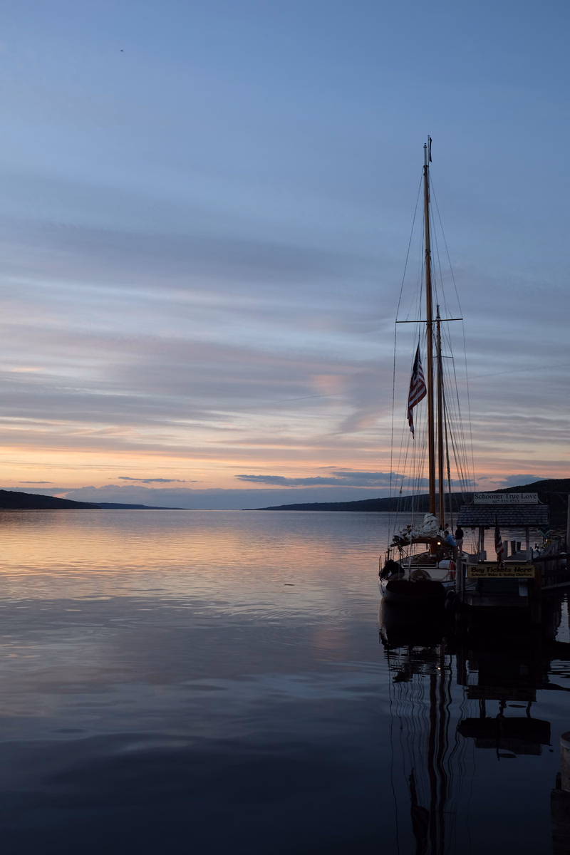 A sailboat with an American flag is visible on the water during a colorful sunset over the ocean.
