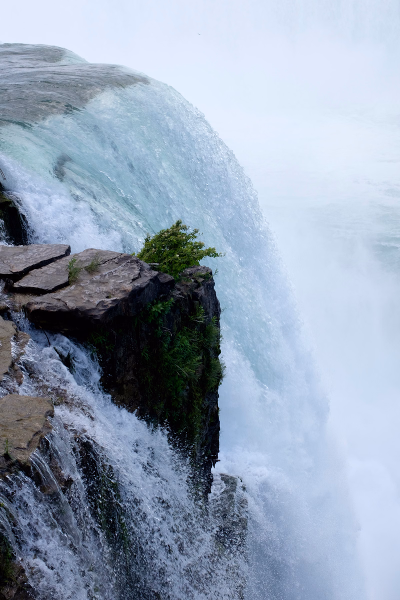 A powerful waterfall cascades over dark rocks into a misty white pool.