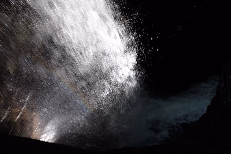 A powerful waterfall creates a massive plume of white spray and mist cascading into a dark pool below.