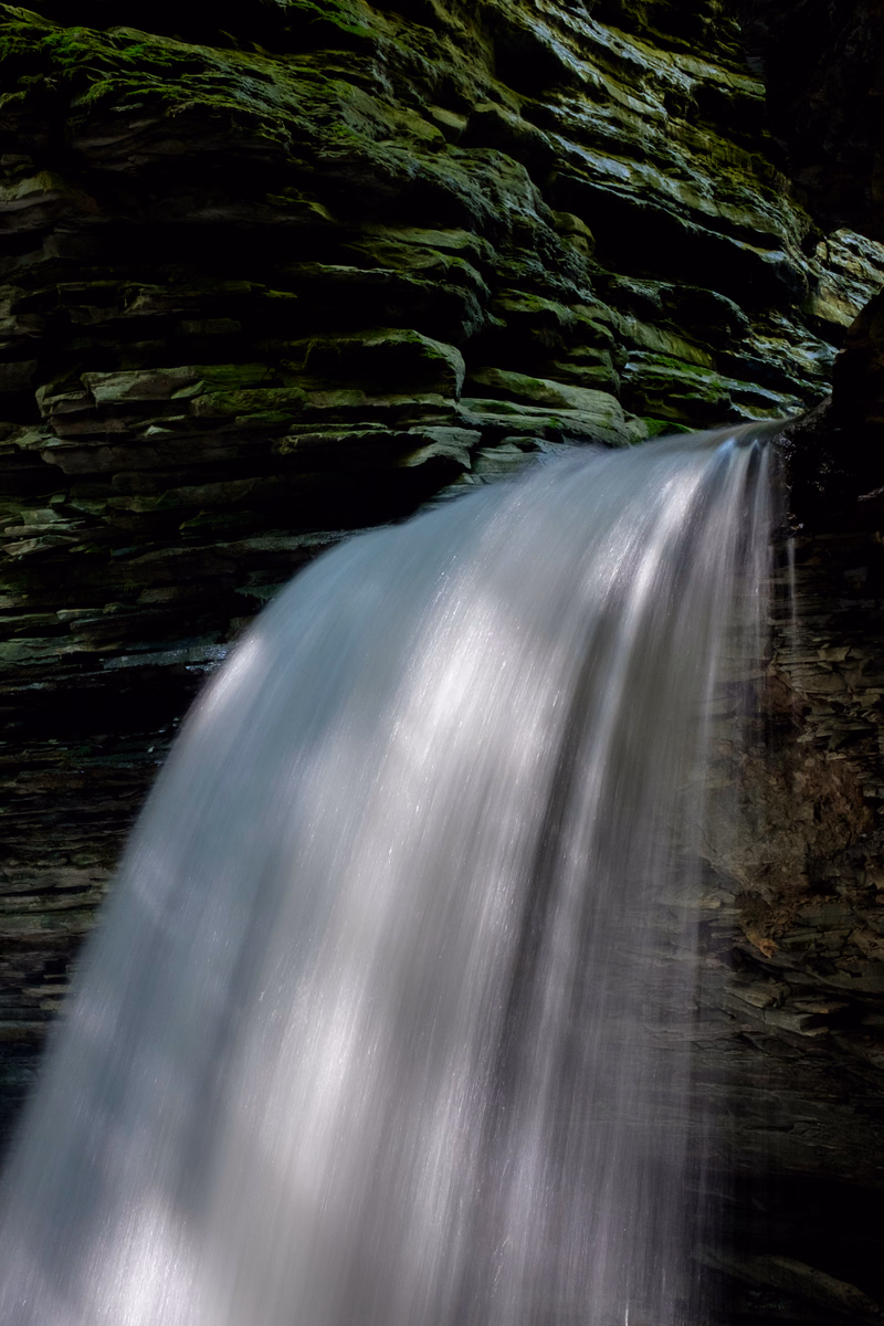 A long exposure photograph captures a smooth, flowing waterfall cascading over dark, layered rocks.