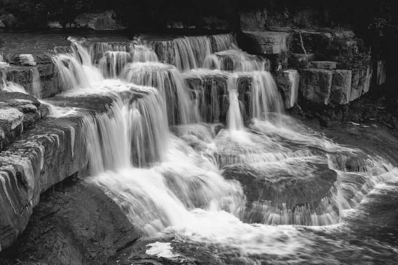 A black and white photograph of a waterfall cascading over rocky terrain in Trumansburg, New York, United States.