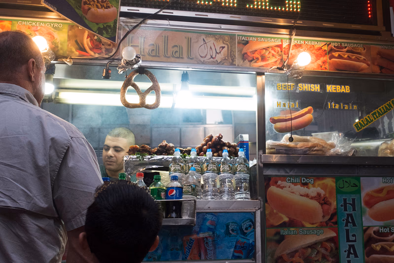 A food stand in a busy street with people eating and drinking.