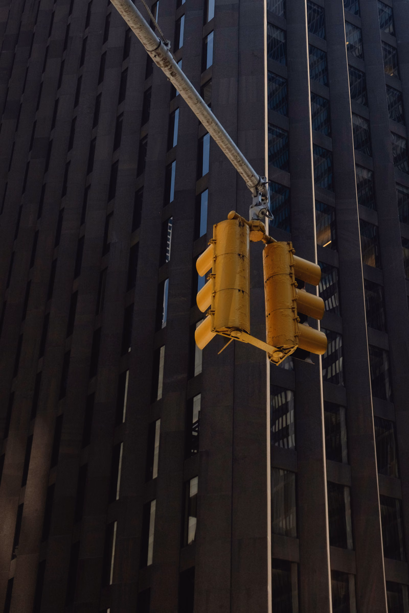 A yellow traffic light hangs from a pole against the dark facade of a tall modern building.