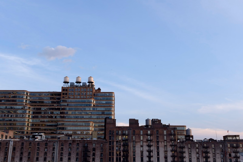 A view of several large apartment buildings with visible rooftops against a bright, pale blue sky.