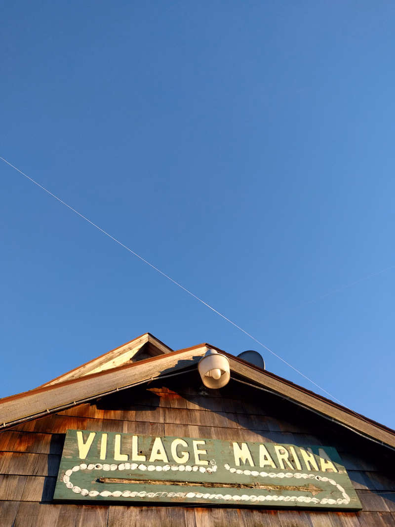 A wooden building with a sign that reads "VILLAGE MARINA" is visible against a clear blue sky.