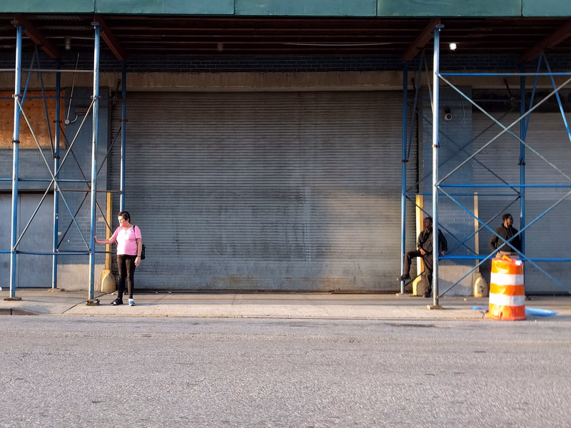 Two people stand near a large, closed roll-up door of an industrial building, with construction scaffolding visible.