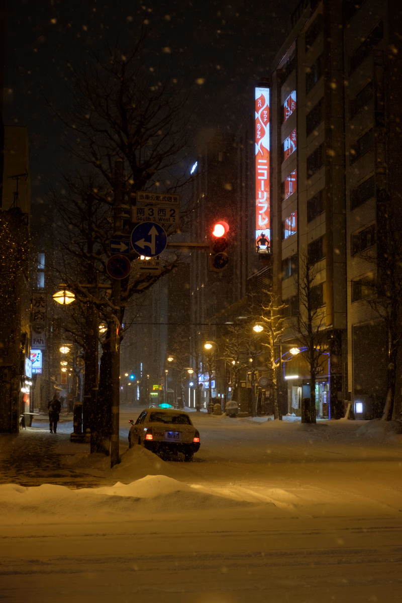 A snowy night in Sapporo, Japan, with a car waiting at a red light.