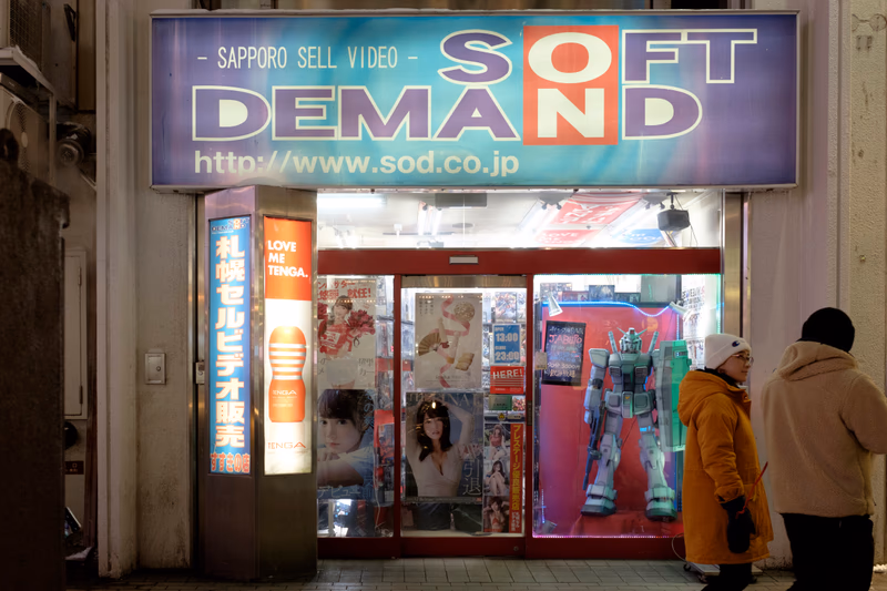 A storefront with a robot and people in front of it, with a sign advertising a video store.