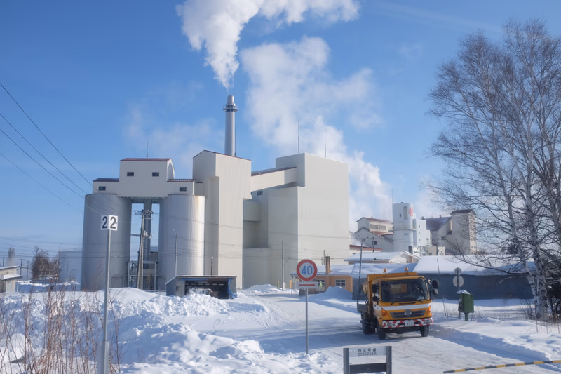 A wintery scene in Hokkaido, Japan, featuring a factory and a truck driving through a snowy landscape.