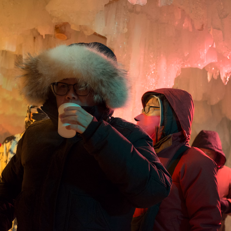 Three people bundled up in winter gear, including fur-trimmed hats, stand in front of a snowy, icy background.