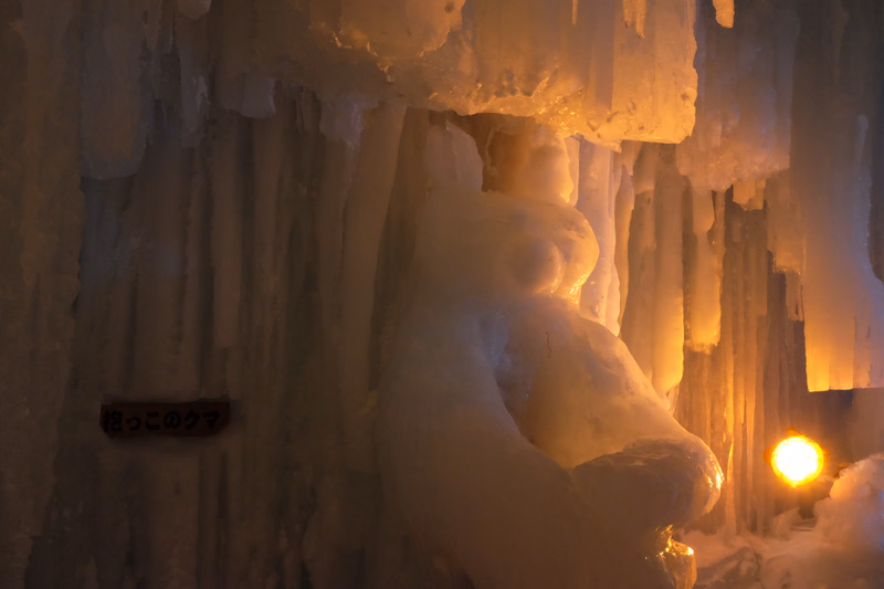 A large ice sculpture of a polar bear stands against a backdrop of hanging icicles, with a sign reading "ねっこ の クマ" visible.