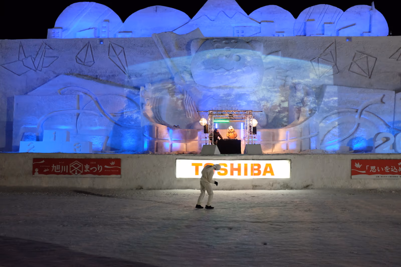 A man in a white suit walking in front of an ice sculpture.