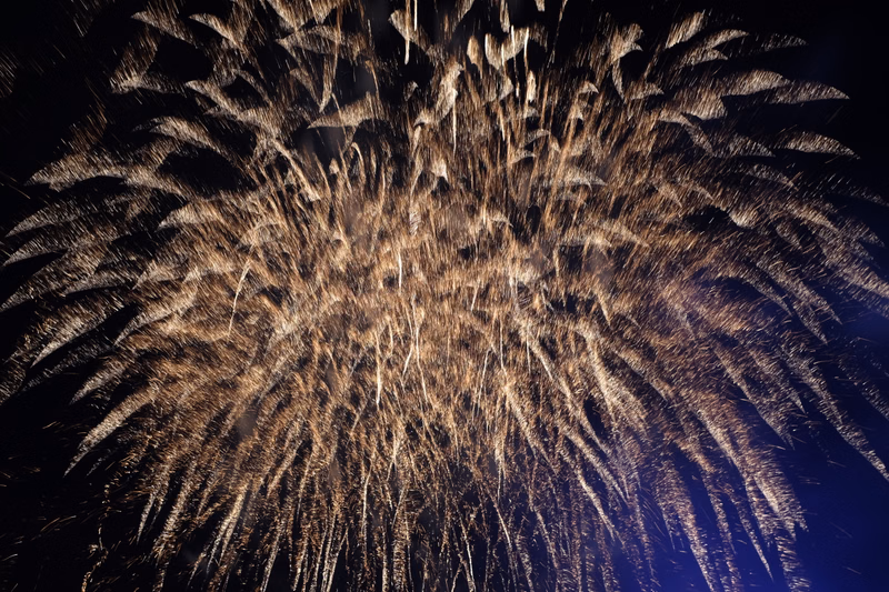 A large, bright burst of golden fireworks illuminates the dark night sky during a celebration.