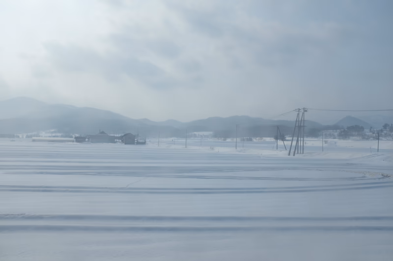 A snowy landscape with a mountain in the background and a building in the middle of the field.