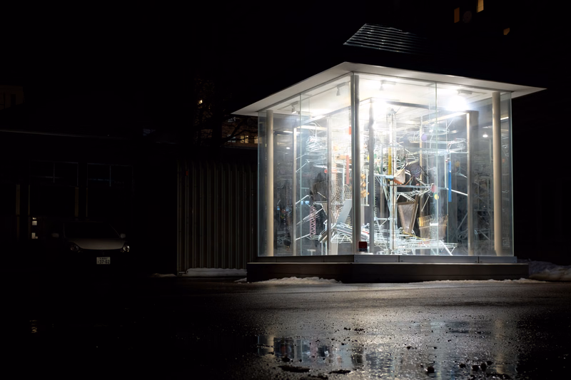 A modern glass building illuminated at night, showcasing an interior display of abstract wireframe structures.