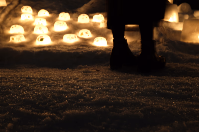 A nighttime scene with a person standing in front of a group of glowing candles on snow.