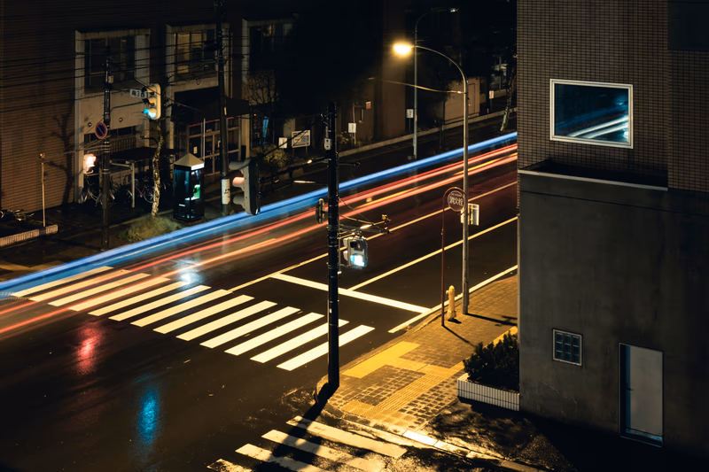 A nighttime cityscape with light trails and a zebra crossing.