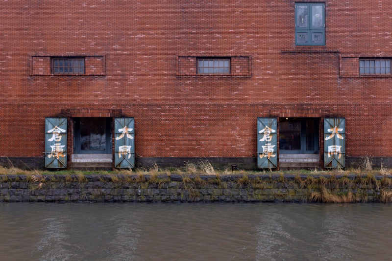 A red brick building with large windows and signs reading "金花庵" and "大雨" along the waterfront.