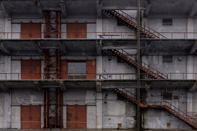 A photograph of an old industrial building with rusty metal stairs and doors.