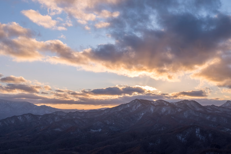 A view of dark mountains under a dramatic sky filled with clouds during sunset.