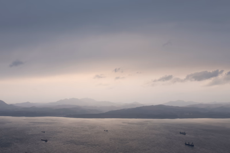 A serene seascape with a calm sea and distant mountains under a cloudy sky.