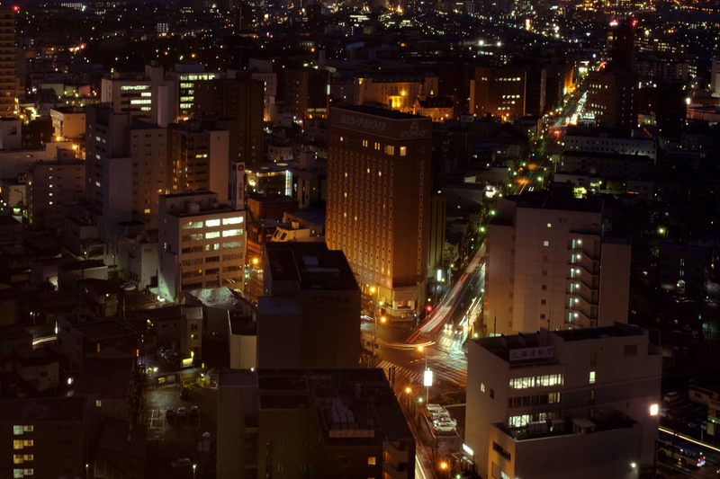 A nighttime cityscape view showing numerous illuminated buildings and streets in a dense urban area.