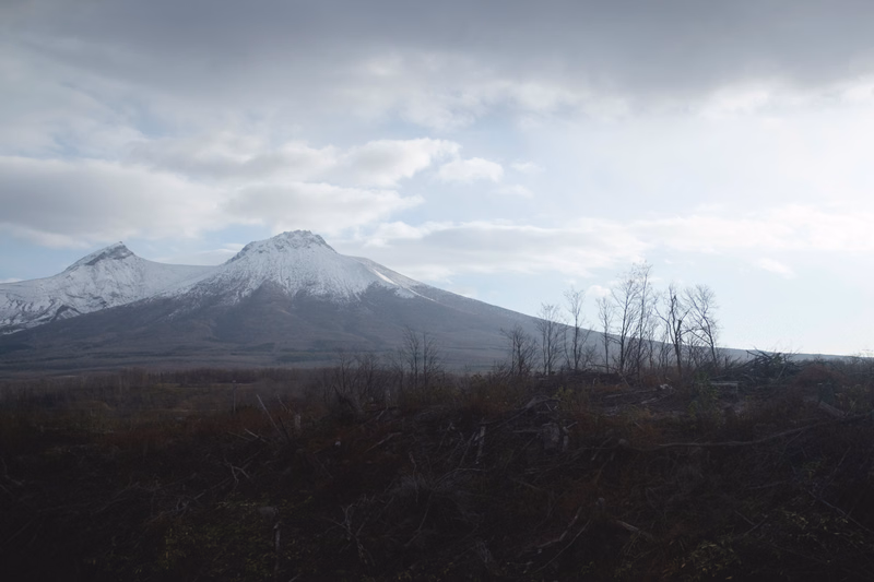 A wide landscape view of snow-capped mountains under a cloudy, overcast sky.
