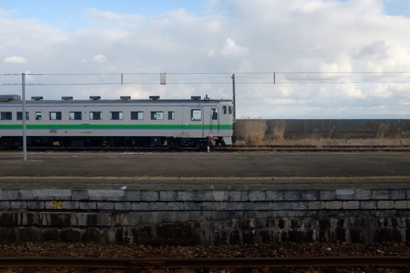 A green and white passenger train is stopped at a railway platform under a cloudy sky.