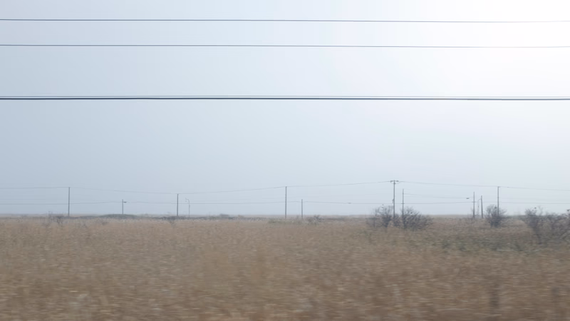 A photo of a vast, open field with power lines stretching across it and a hazy horizon.
