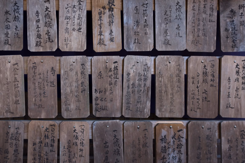A collection of weathered wooden planks, each inscribed with vertical Japanese text, stacked in rows.
