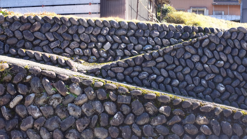 A tiered dry stone retaining wall made of rounded grey stones slopes across a landscaped area.