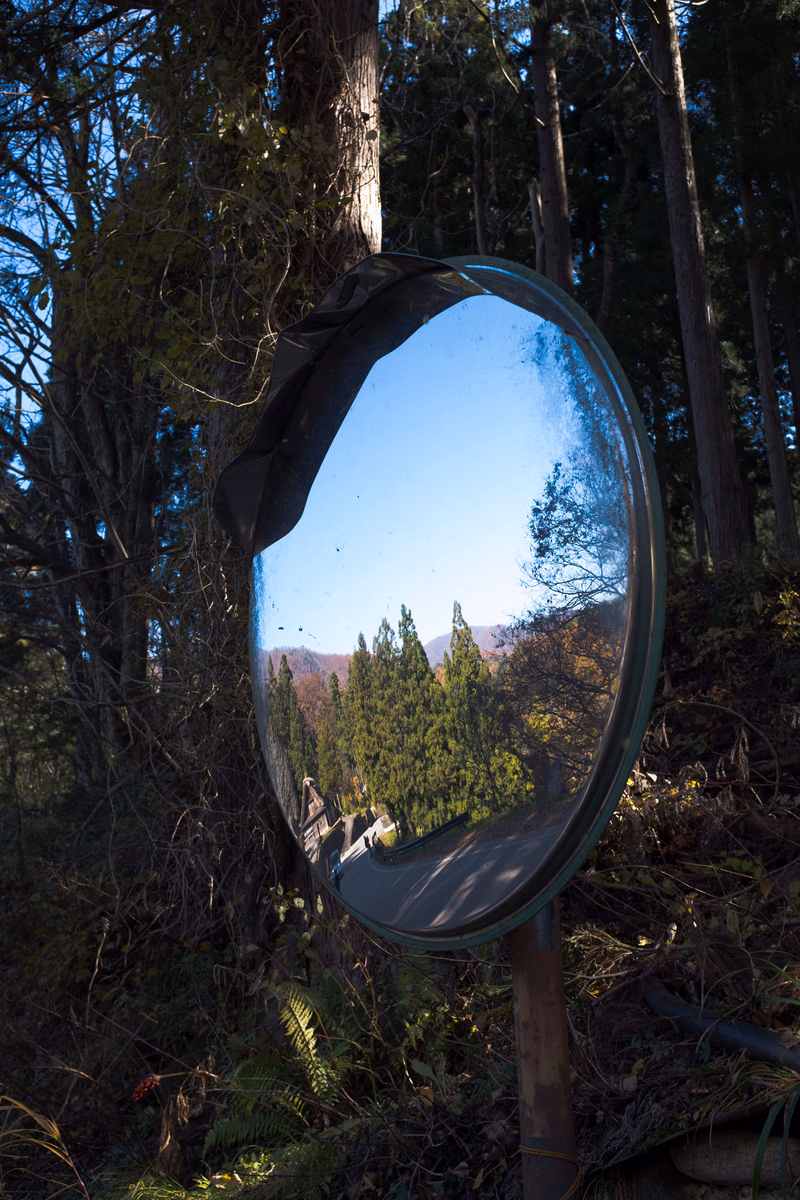 A large, round outdoor mirror reflects a clear blue sky, green trees, and distant hills.