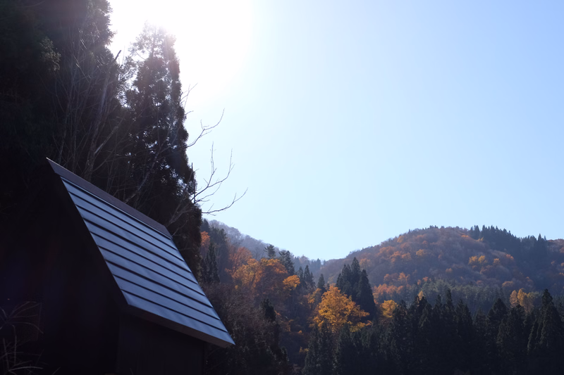 A modern house with a slanted roof is visible against a bright blue sky, overlooking hills covered in autumn foliage.