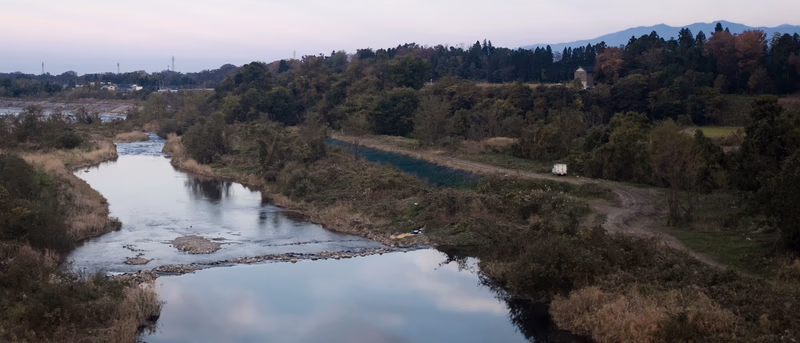 A serene river running through a lush forest, with a small path and a house nestled among the trees.