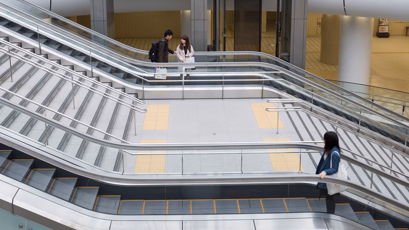 A photo of a modern building with escalators, showing people interacting and using the space.