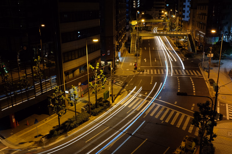 Long exposure photograph of light trails from vehicle traffic moving through a city street at night.