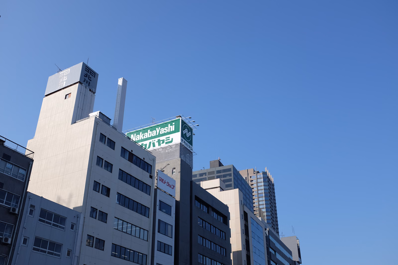 A cluster of modern office buildings under a clear blue sky, one sign reads "Nakabayashi".