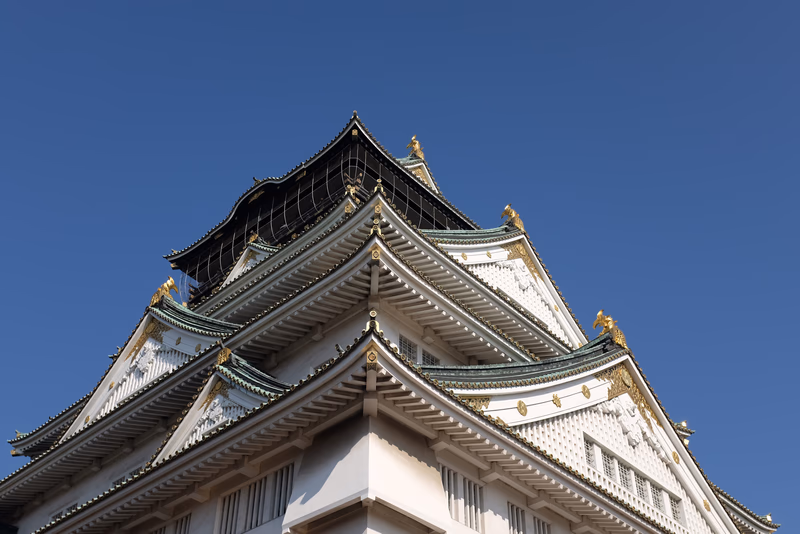 A photograph of a traditional Japanese castle taken from a high angle, showcasing its intricate details and the serene blue sky in the background.