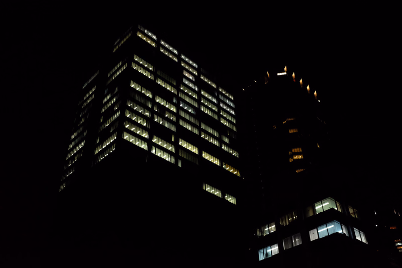 Two illuminated modern high-rise buildings stand against a dark night sky.