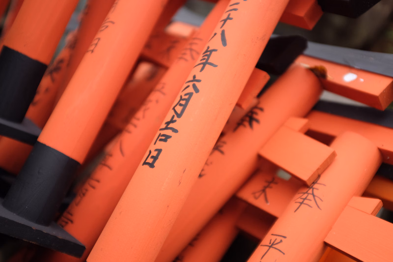 A close-up view of several bright orange wooden poles with black caps, featuring Japanese text that reads "八年六月廿日" on the central pole.