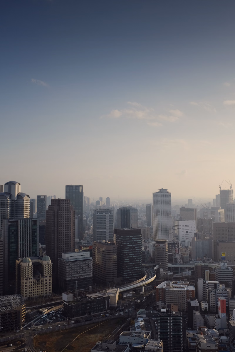 A wide cityscape view of numerous high-rise buildings under a pale blue and white sky during daylight.