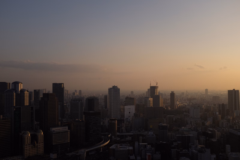 A panoramic view of a dense city skyline during sunset, with numerous high-rise buildings silhouetted against the warm sky.