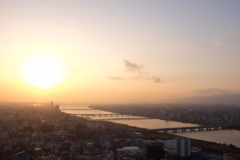 A bright sunrise illuminates a wide cityscape featuring a river spanned by multiple bridges.
