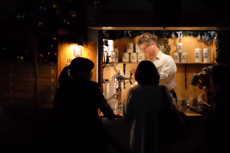 A bartender serves drinks to several patrons inside a dimly lit pub, with beer taps visible behind the counter.