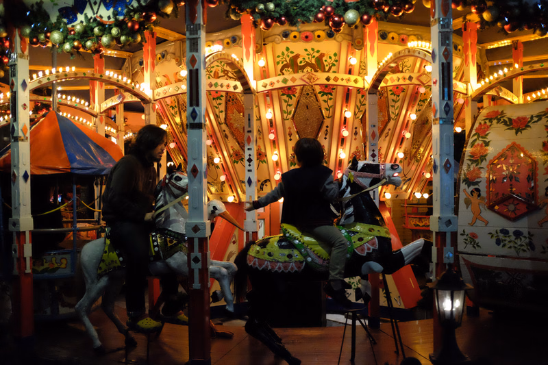 People ride a brightly decorated indoor carousel with ornate, colorful panels and lights.